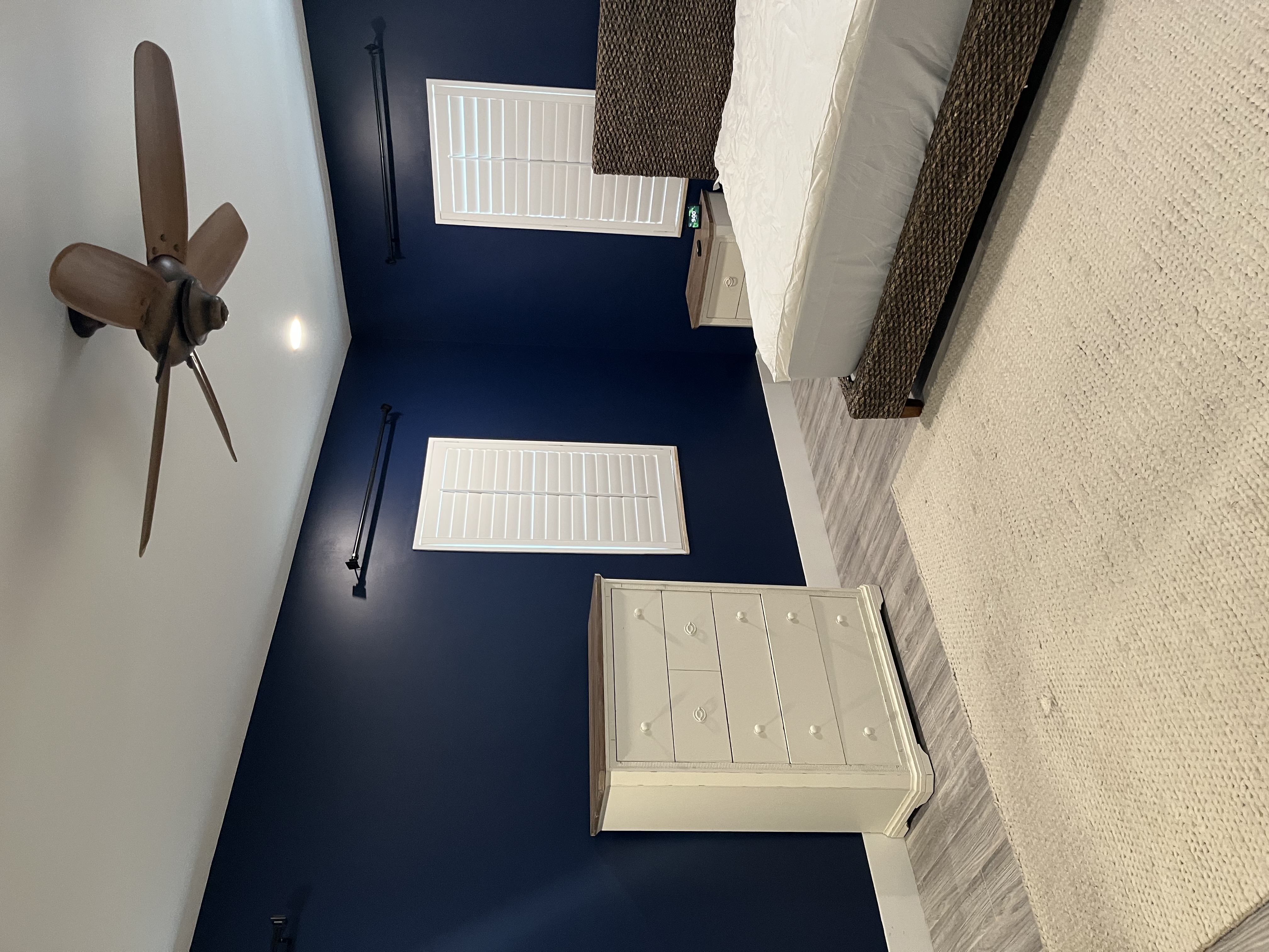 Finished bedroom painting job showing the bed wall with deep blue paint and white window trim