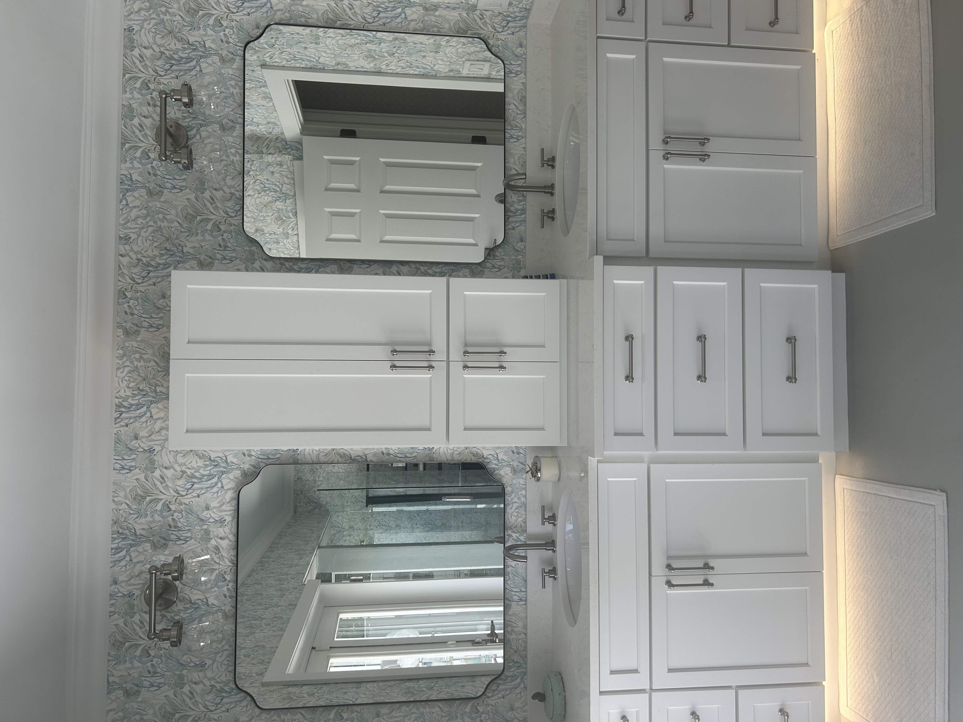 Finished bathroom with dual mirrors installed above a double vanity and floral wallpaper backdrop