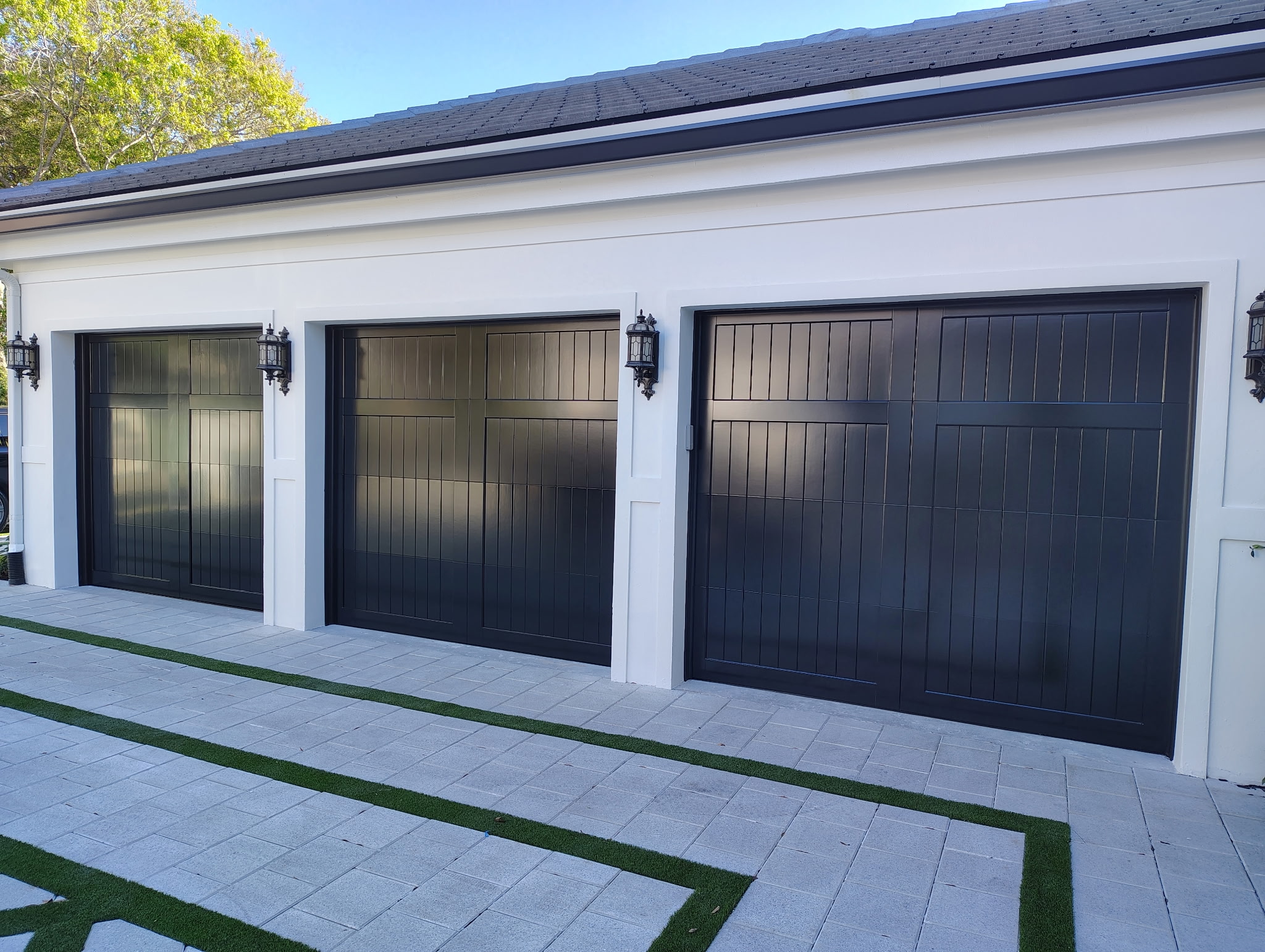 Finished three-bay garage with matching black carriage-style garage doors and white exterior walls
