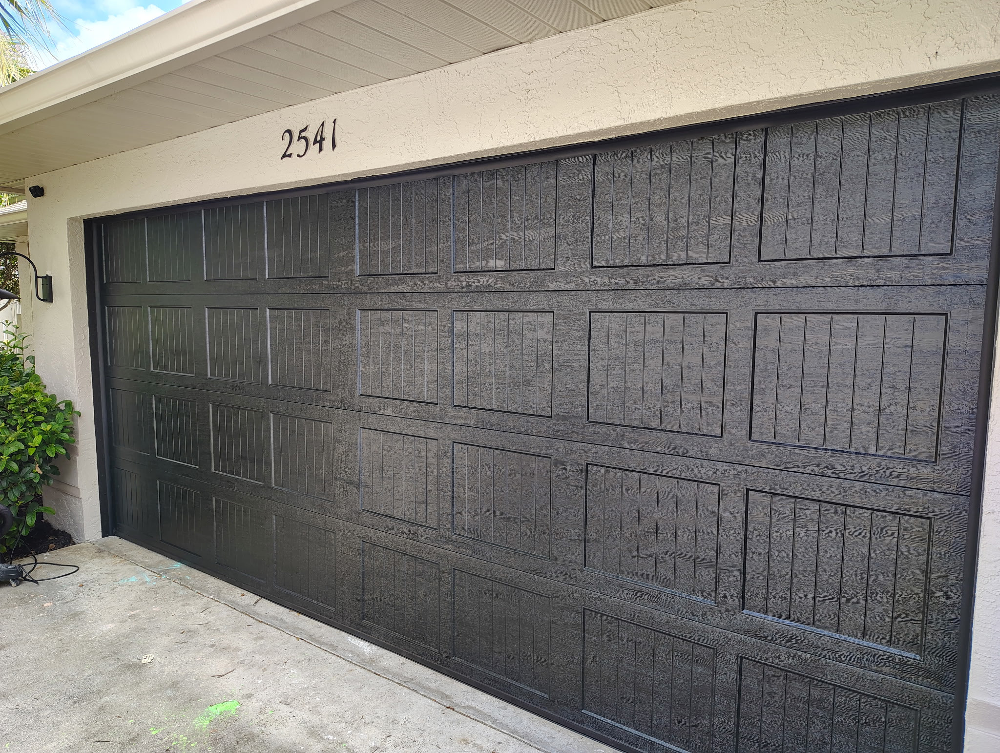 Finished black paneled garage door installed on a residential home exterior