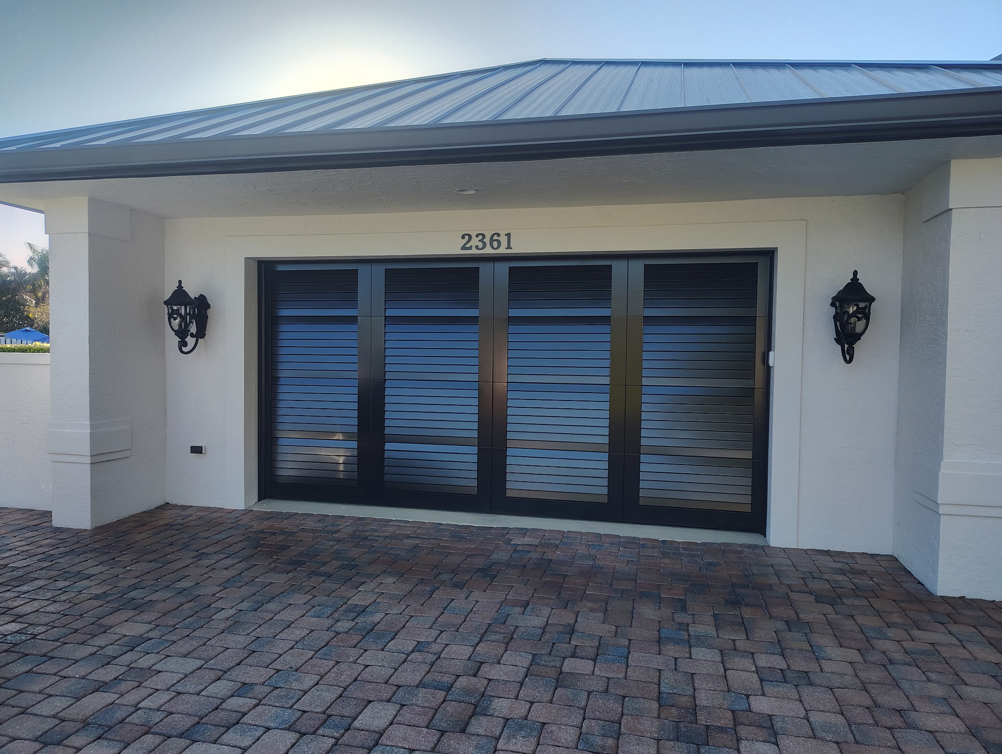 Finished modern black garage door with horizontal glass inserts on a white home exterior