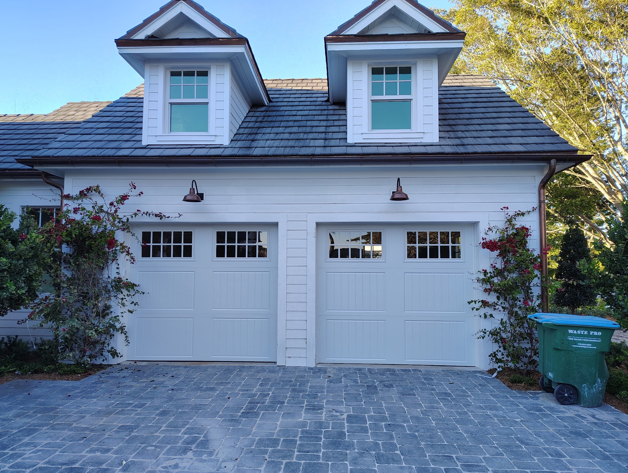 Finished pair of white carriage-style garage doors on a large home with dormer windows above