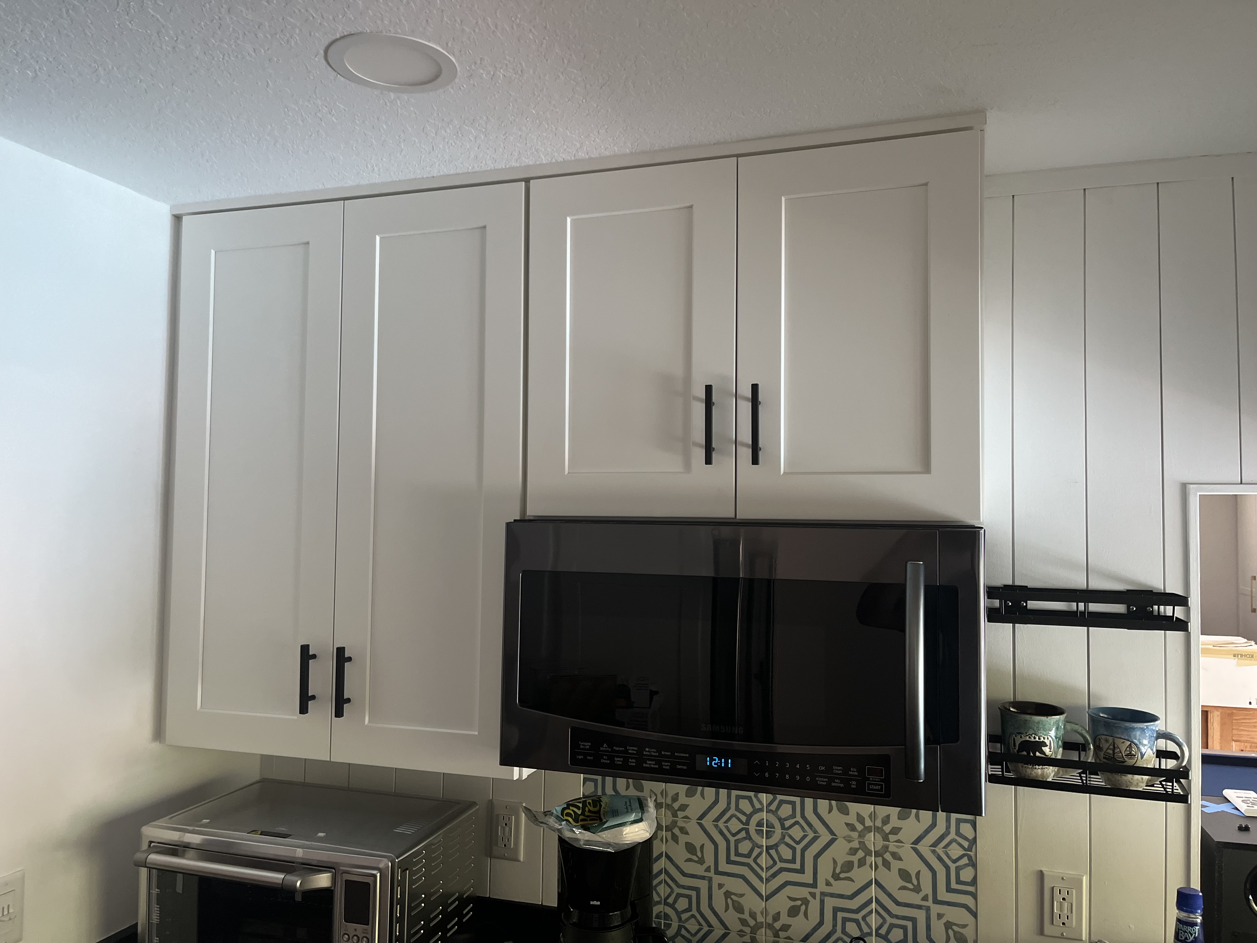 Finished kitchen cabinet installation with white shaker-style upper cabinets above the microwave