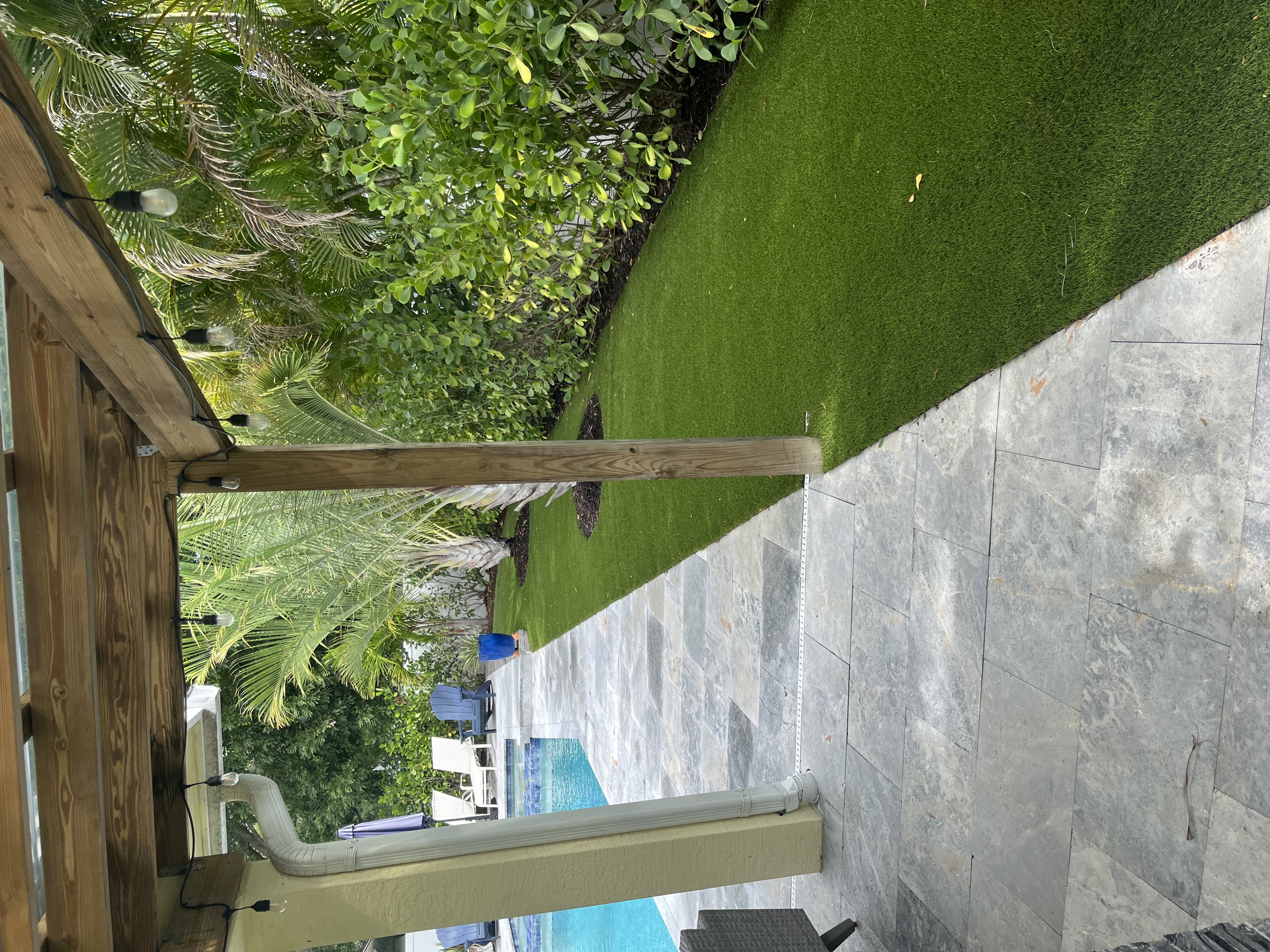 Finished artificial turf installed beside a pool patio with tropical landscaping