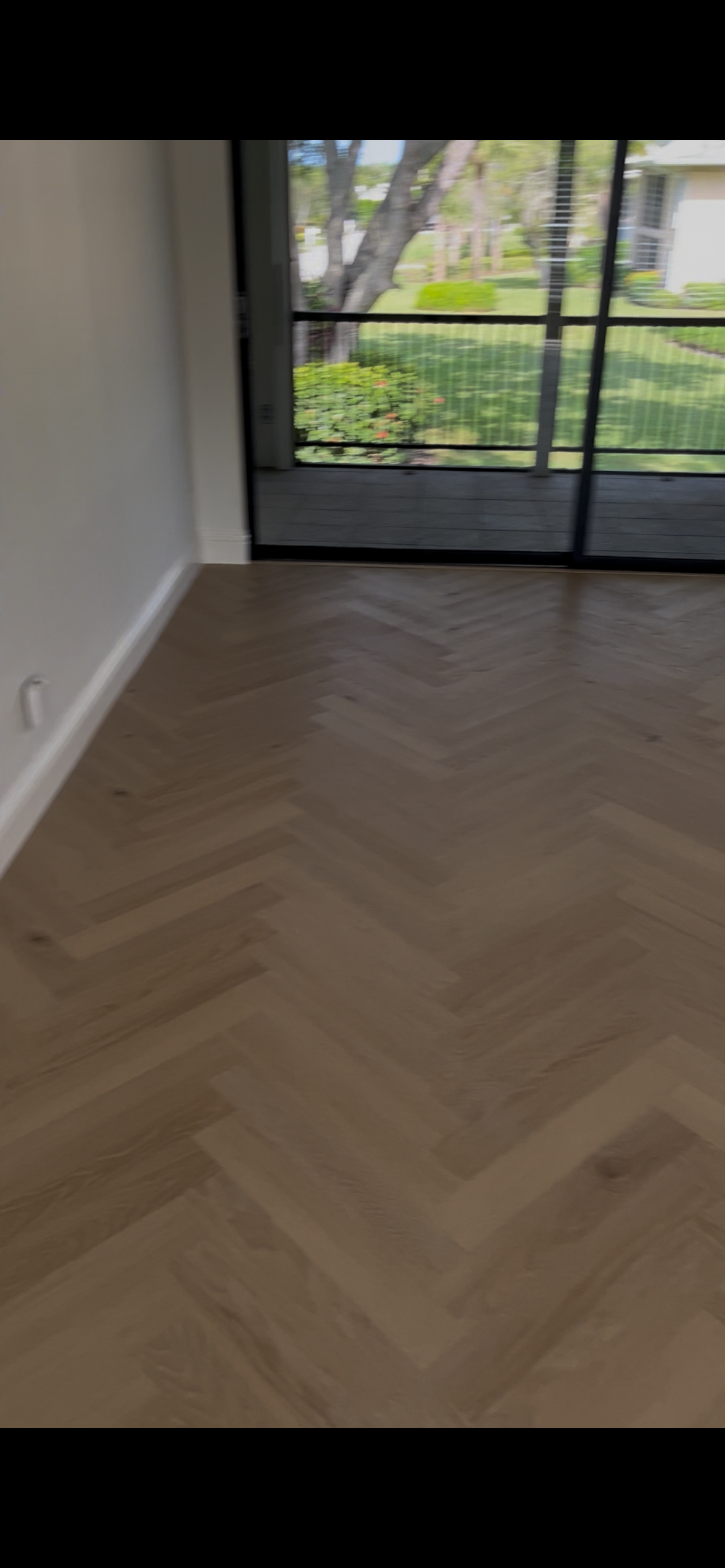 Finished herringbone wood floor installed in the completed room beside large sliding glass doors